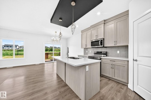 Modern kitchen featuring light wood-finish cabinetry, stainless steel appliances, a center island with a white countertop, and a geometric tile backsplash - 8823 Carson Way Sw, Edmonton, AB - Indoor Photo Showing Kitchen With Upgraded Kitchen
