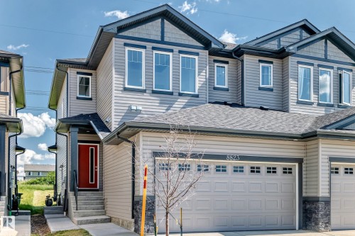 Modern facade with gray horizontal siding, dark trim accents, a vibrant red entry door, a covered porch, and an attached garage - 8823 Carson Way Sw, Edmonton, AB - Outdoor With Facade