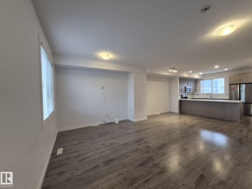 Open-concept living space with wood-finish flooring, recessed lighting, white walls, and a kitchen featuring stainless steel appliances and wood-finish cabinetry - Edmonton, AB - Indoor