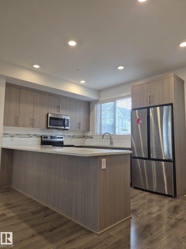 Recessed lighting, wood-finish flooring, stainless steel appliances, kitchen island with countertop, and white tile backsplash - Edmonton, AB - Indoor Photo Showing Kitchen