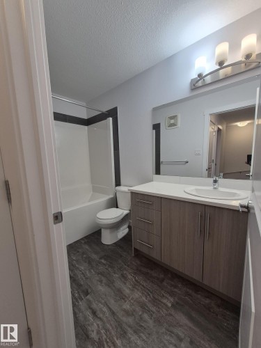Bathroom featuring a wood-finish vanity with a white countertop, an integrated sink, a rectangular mirror, and a wall-mounted light fixture - Edmonton, AB - Indoor Photo Showing Bathroom