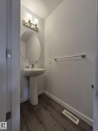 Pedestal sink, round wall-mounted mirror, brushed nickel wall sconce, and wood-finish flooring - Edmonton, AB - Indoor Photo Showing Bathroom