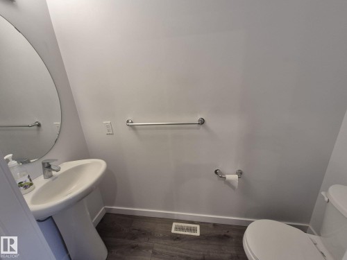 Pedestal sink with a chrome faucet, large circular mirror, and wood-finish flooring - Edmonton, AB - Indoor Photo Showing Bathroom