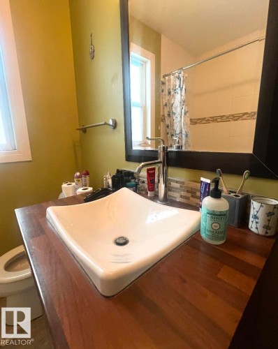 Vessel sink with a chrome faucet, wood-finish countertop, and decorative tile backsplash - 9828 84 Avenue Nw, Edmonton, AB - Indoor Photo Showing Bathroom