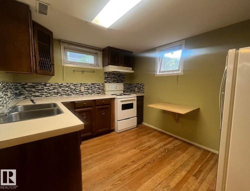 Wood-finish flooring, mosaic tile backsplash, double basin stainless steel sink, and a wall-mounted folding table - 9828 84 Avenue Nw, Edmonton, AB - Indoor Photo Showing Kitchen With Double Sink