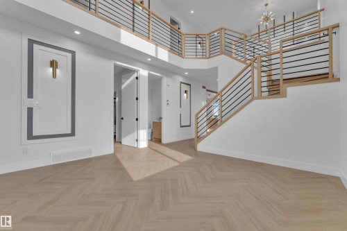 Herringbone wood-finish flooring, two-story open concept design, modern staircase with black rod balusters and wood handrails, recessed lighting, and decorative wall sconces - 465 Crystal Creek Link, Leduc, AB - Indoor Photo Showing Other Room