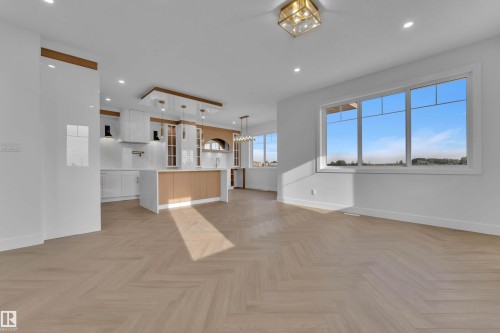 Light wood-finish herringbone flooring, kitchen island with wood-finish paneling, white cabinetry, recessed lighting, and a contemporary ceiling fixture - 465 Crystal Creek Link, Leduc, AB - Indoor Photo Showing Kitchen