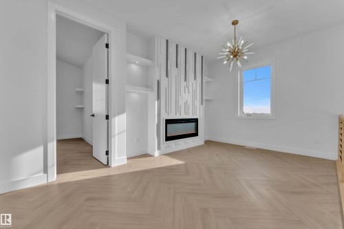 Herringbone wood-finish flooring, built-in electric fireplace, integrated shelving with accent lighting, contemporary chandelier, and a white interior door with black hardware - 465 Crystal Creek Link, Leduc, AB - Indoor Photo Showing Other Room With Fireplace