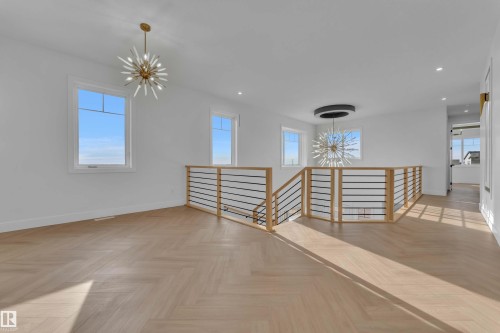 Herringbone wood-finish flooring, contemporary open stair railing with wood and metal accents, recessed lighting, and multiple windows - 465 Crystal Creek Link, Leduc, AB - Indoor Photo Showing Other Room