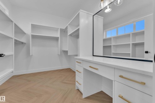 Walk-in closet with extensive built-in shelving, herringbone wood-finish flooring, built-in vanity with quartz countertop, large vanity mirror, and overhead decorative lighting - 465 Crystal Creek Link, Leduc, AB - Indoor With Storage