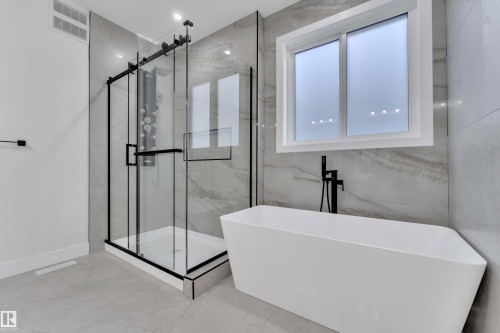 Freestanding soaking tub with matte black floor-mounted filler, glass-enclosed shower with matte black fixtures, and large-format wall and floor tiling - 465 Crystal Creek Link, Leduc, AB - Indoor Photo Showing Bathroom