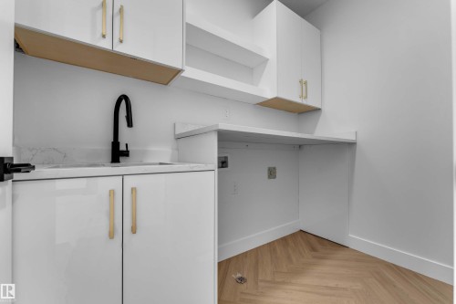 White cabinetry with gold-tone hardware, undermount sink with matte black faucet, light-toned countertop, open shelving, and herringbone wood-finish flooring - 465 Crystal Creek Link, Leduc, AB - Indoor