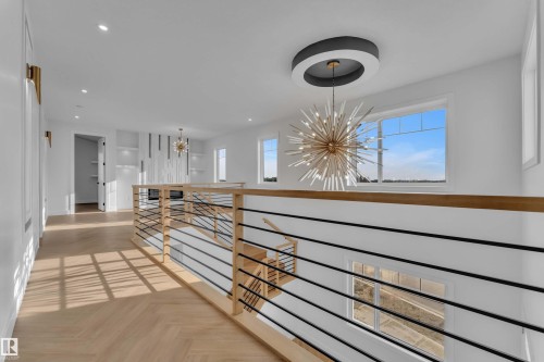 Modern open-concept landing featuring light wood-finish flooring, contemporary stair railing with wood handrails and black metal spindles, and a distinctive sputnik-style chandelier - 465 Crystal Creek Link, Leduc, AB - Indoor Photo Showing Other Room