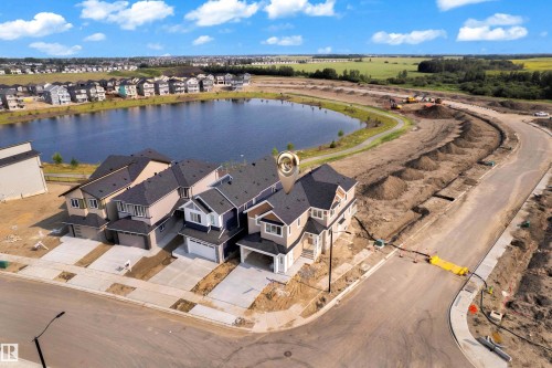 Newly constructed residential property featuring a modern architectural design, attached garage, and a paved driveway - 465 Crystal Creek Link, Leduc, AB - Outdoor With Body Of Water With View