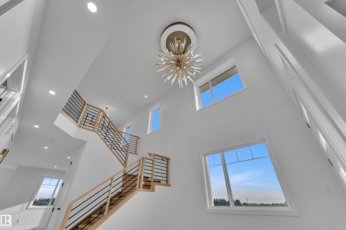 Two-story entry with a contemporary chandelier, multiple large windows, recessed lighting, and a modern wood staircase with black iron balusters - 465 Crystal Creek Link, Leduc, AB - Indoor Photo Showing Other Room
