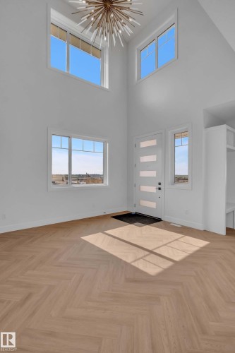Two-story entry with multiple windows, herringbone-pattern wood-finish flooring, a modern front door, and a prominent chandelier - 465 Crystal Creek Link, Leduc, AB - Indoor Photo Showing Other Room