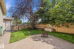 Expansive backyard featuring a concrete patio, mature trees, a wooden privacy fence, and a storage shed with an overhead door - 