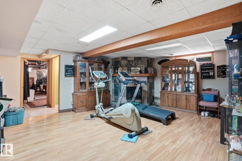 Spacious lower-level room featuring wood-finish flooring, a stone-faced fireplace, and exposed wood beams - 5702 52 Avenue, Beaumont, AB - Indoor Photo Showing Gym Room