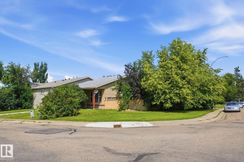 Corner lot property featuring exterior siding, mature trees, and a green lawn - 5702 52 Avenue, Beaumont, AB - Outdoor