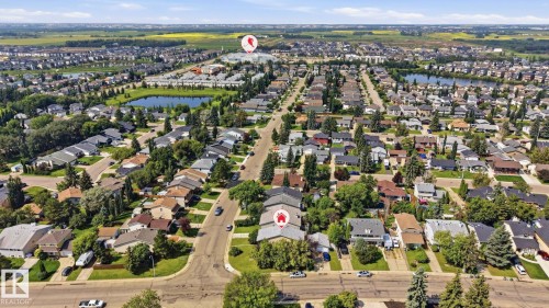 Aerial view showcasing a residential neighborhood with numerous single-family homes, mature trees, and a visible pond feature - 5702 52 Avenue, Beaumont, AB - Outdoor With View