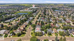 Aerial view showcasing a residential neighborhood with numerous single-family homes, mature trees, and a visible pond feature - 