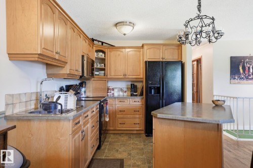 Kitchen featuring wood-finish cabinetry, black appliances, solid surface countertops, and an island with seating - 5702 52 Avenue, Beaumont, AB - Indoor Photo Showing Kitchen