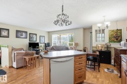 Open-concept living area featuring wood-finish flooring, a kitchen island with integrated dishwasher, and a chandelier lighting fixture - 
