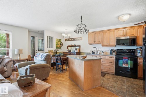 Open-concept living space featuring wood-finish flooring, a kitchen island with stone-look countertop, light wood cabinetry, and stainless steel appliances - 5702 52 Avenue, Beaumont, AB - Indoor Photo Showing Kitchen