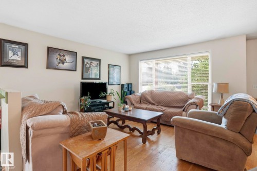 Living area featuring wood-finish flooring and a large window with horizontal blinds - 5702 52 Avenue, Beaumont, AB - Indoor Photo Showing Living Room