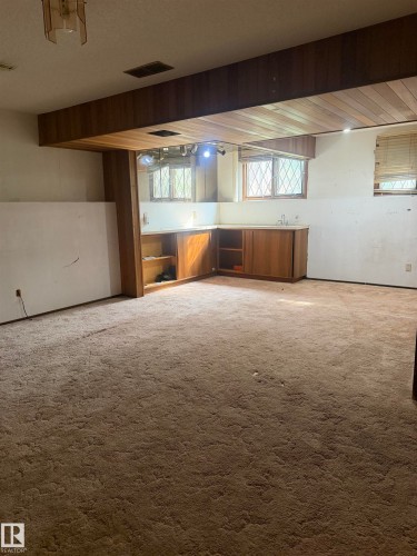 Spacious basement recreation area featuring exposed wood-beam ceiling, carpeted flooring, built-in cabinetry with wood finishes, and multiple windows providing natural light - 9223 172 Avenue Nw, Edmonton, AB 