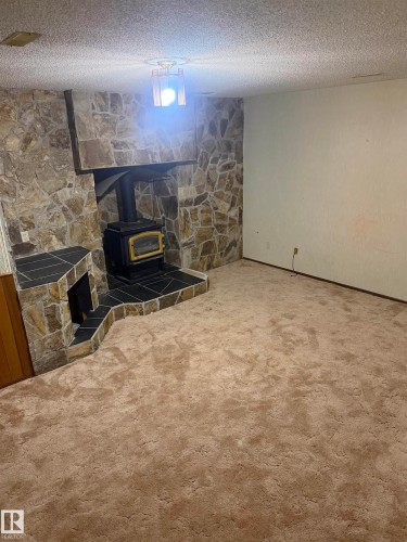 Finished basement recreation space featuring carpeted flooring, stone accent wall with wood-burning stove insert, and neutral wall finishes - 9223 172 Avenue Nw, Edmonton, AB 