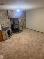 Finished basement recreation space featuring carpeted flooring, stone accent wall with wood-burning stove insert, and neutral wall finishes - 