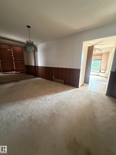 Spacious living area featuring neutral carpeting, two-tone wood-finish wainscoting, and pendant lighting - 9223 172 Avenue Nw, Edmonton, AB 