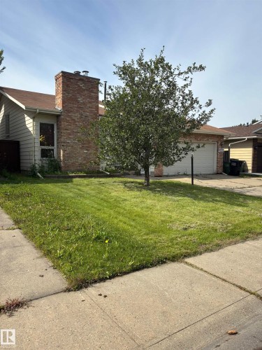 Brick chimney with a metal cap, attached garage with a white door, and a concrete driveway - 9223 172 Avenue Nw, Edmonton, AB 