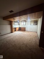 Spacious open-concept room featuring exposed wood-beam ceiling, recessed lighting, carpet flooring, and built-in cabinetry with wood finishes - 