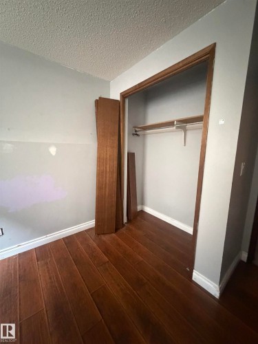 Spacious bedroom featuring rich wood-finish flooring, white painted walls, and a generous walk-in closet with wooden framing and built-in hanging rod - 9223 172 Avenue Nw, Edmonton, AB 