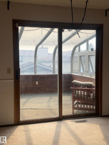 Sliding glass doors with dark wood frames opening to a covered outdoor space featuring exposed beam ceiling, metal railings, and wood-finish decking - 9223 172 Avenue Nw, Edmonton, AB 