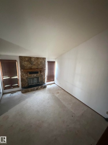 Spacious living area featuring a stone fireplace with integrated hearth, vaulted ceiling, and abundant natural light from multiple windows - 9223 172 Avenue Nw, Edmonton, AB 