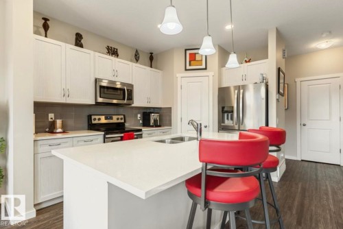 Kitchen featuring white cabinetry, stainless steel appliances, a white island, and wood-finish flooring - 12737 205 Street Nw, Edmonton, AB - Indoor Photo Showing Kitchen With Double Sink