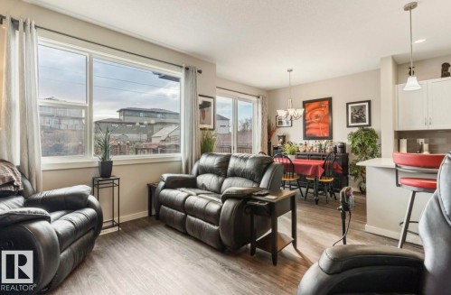 Spacious open-concept living area featuring wood-finish flooring, large windows, recessed lighting, a dining area with a chandelier, and a kitchen bar with pendant lighting - 12737 205 Street Nw, Edmonton, AB - Indoor Photo Showing Living Room