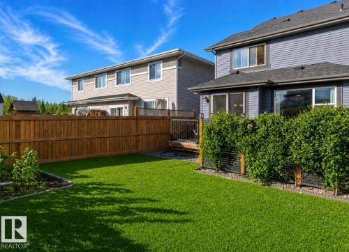 Expansive turf lawn with a wooden privacy fence, established shrubbery, and a compact wooden deck - 12737 205 Street Nw, Edmonton, AB - Outdoor