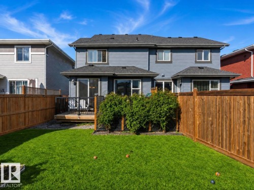 Fenced backyard with a grassy lawn, wood deck, and mature privacy shrubs - 12737 205 Street Nw, Edmonton, AB - Outdoor With Deck Patio Veranda