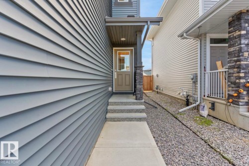 Concrete walkway leading to a glass-paneled entry door, flanked by stone veneer columns and a covered porch - 12737 205 Street Nw, Edmonton, AB - Outdoor