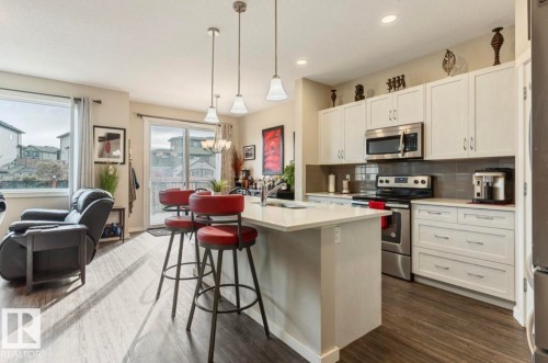 Modern kitchen featuring white cabinetry, stainless steel appliances, a center island with pendant lighting, and wood-finish flooring - 12737 205 Street Nw, Edmonton, AB - Indoor Photo Showing Kitchen With Upgraded Kitchen
