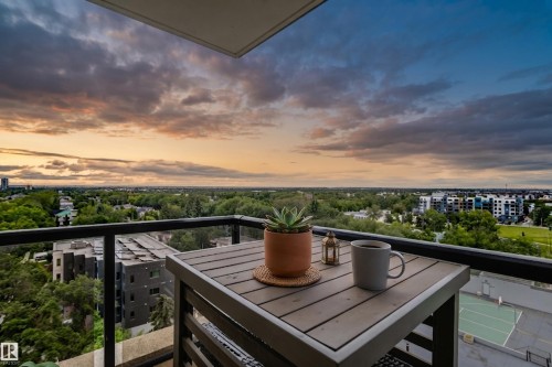 Balcony featuring a slatted table, metal railing, and glass balustrade overlooking a distant cityscape and green spaces - #1002 10149 Saskatchewan Dr Nw, Edmonton, AB - Outdoor With View