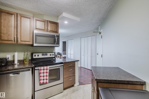 Kitchen featuring wood cabinetry, stainless steel appliances, dark stone-finish countertops, and recessed lighting - #1002 10149 Saskatchewan Dr Nw, Edmonton, AB - Indoor Photo Showing Kitchen