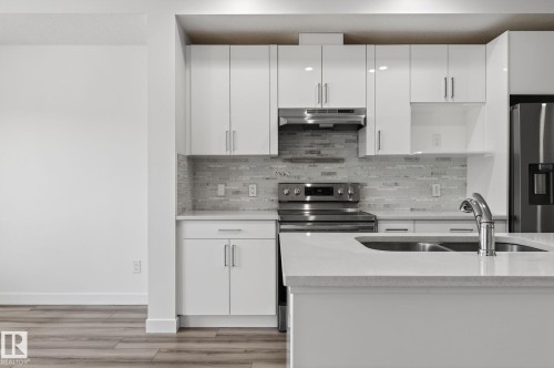 Kitchen featuring white upper and lower cabinetry, a stainless steel range with overhead ventilation, a stainless steel refrigerator, and wood-finish flooring - 4853 Alwood Point(E) Sw, Edmonton, AB - Indoor Photo Showing Kitchen