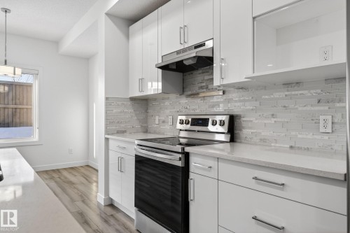 Contemporary kitchen featuring white flat-panel cabinetry, light-toned countertops, a full-height tile backsplash, and stainless steel appliances - 4853 Alwood Point(E) Sw, Edmonton, AB - Indoor Photo Showing Kitchen With Upgraded Kitchen