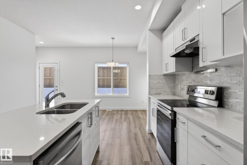 Kitchen featuring white cabinetry, stainless steel appliances, light-toned countertops, tile backsplash, and wood-finish flooring - 4853 Alwood Point(E) Sw, Edmonton, AB - Indoor Photo Showing Kitchen With Double Sink With Upgraded Kitchen