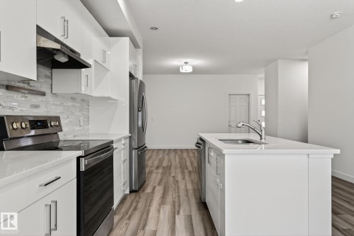 Kitchen featuring white cabinetry, stainless steel appliances, a white island with an undermount sink, and wood-finish flooring - 4853 Alwood Point(E) Sw, Edmonton, AB - Indoor Photo Showing Kitchen